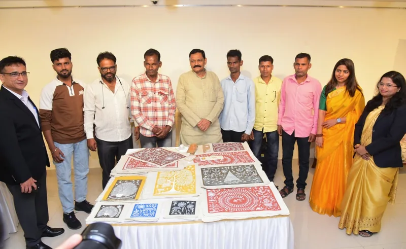 आदि चित्र प्रदर्शनी में चित्रों से सजी मेज़ के पीछे खड़े प्रतिभागी